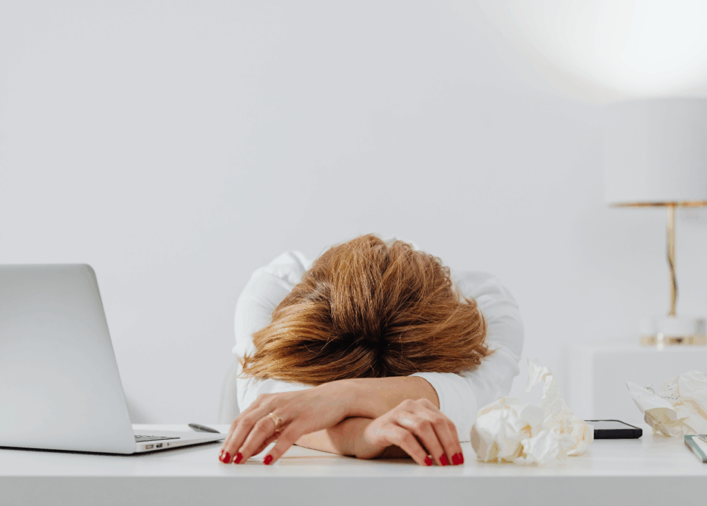 Woman with her head on her desk beside crumpled paper and a laptop, representative of anxiety in high-achievers.