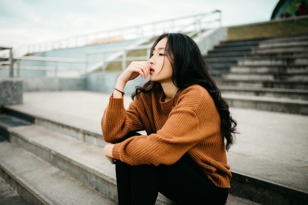 Person sitting on steps outside with their hand on their mouth thinking about DBT skills they can use.